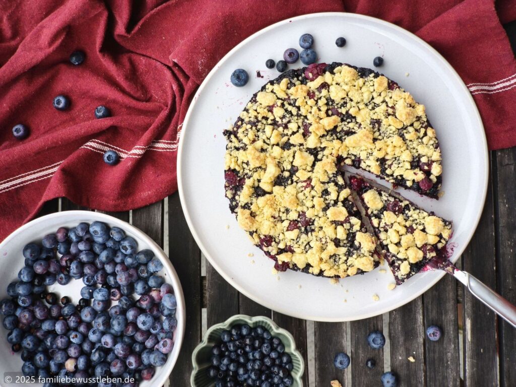 Heidelbeerkuchen und Blaubeeren in Schalen auf Tisch mit roten Küchentuch