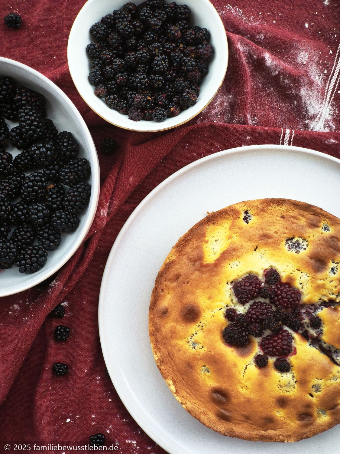 Draufsicht auf einen runden Brombeerkuchen mit Sahneguss und zwei Schalen mit Brombeeren aus dem Wald und aus dem Garten.