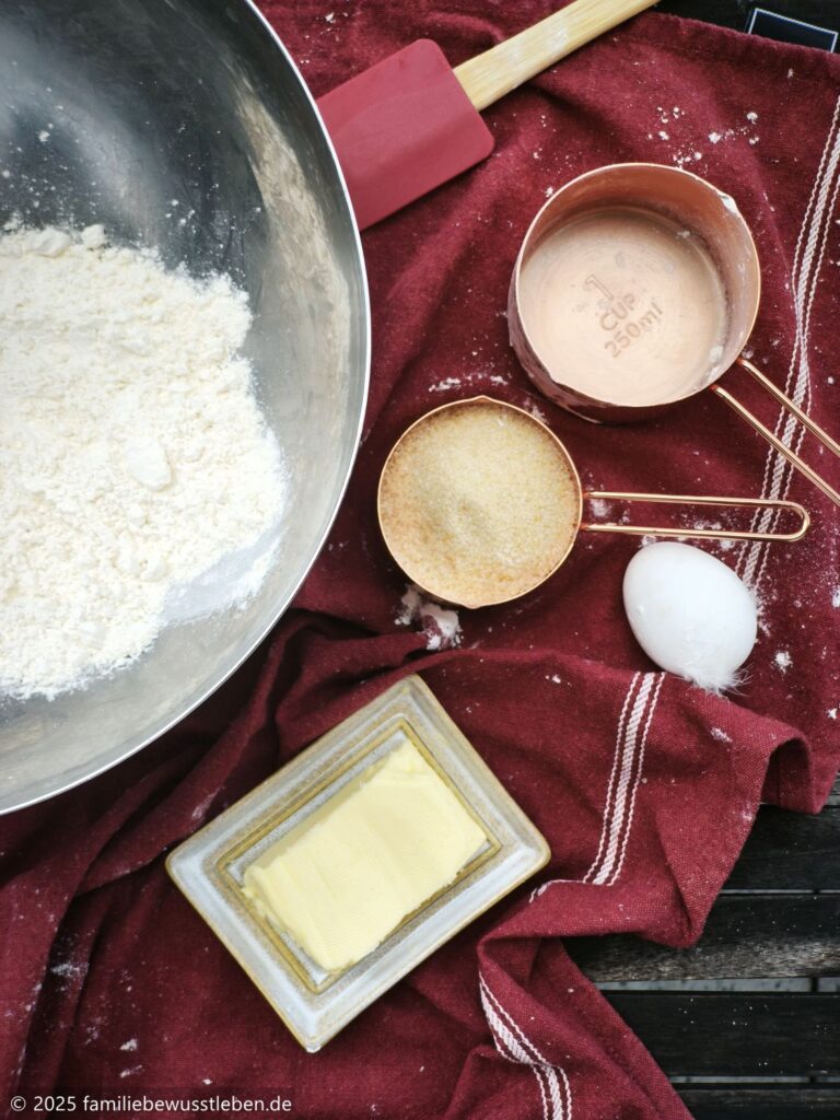 Zutaten für den Teig vom Brombeerkuchen: Mehl in einer Edelstahlschüssel, Zucker, Butter und ein Ei.