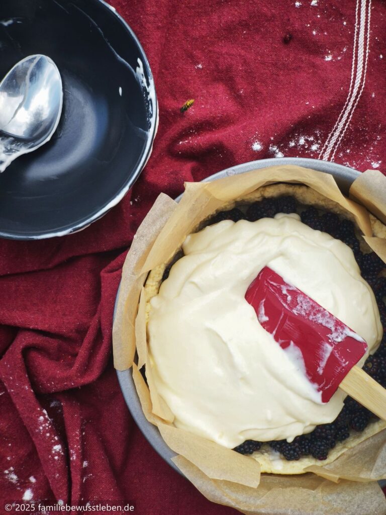 Der Sahneguss wird auf dem Brombeerkuchen verteilt.
