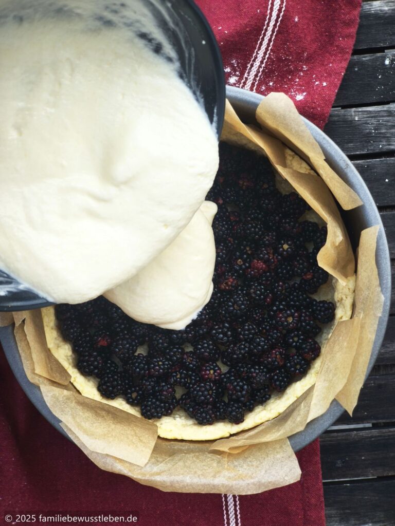 Draufsicht wie der Sahneguss auf den Brombeerkuchen gegeben wird.