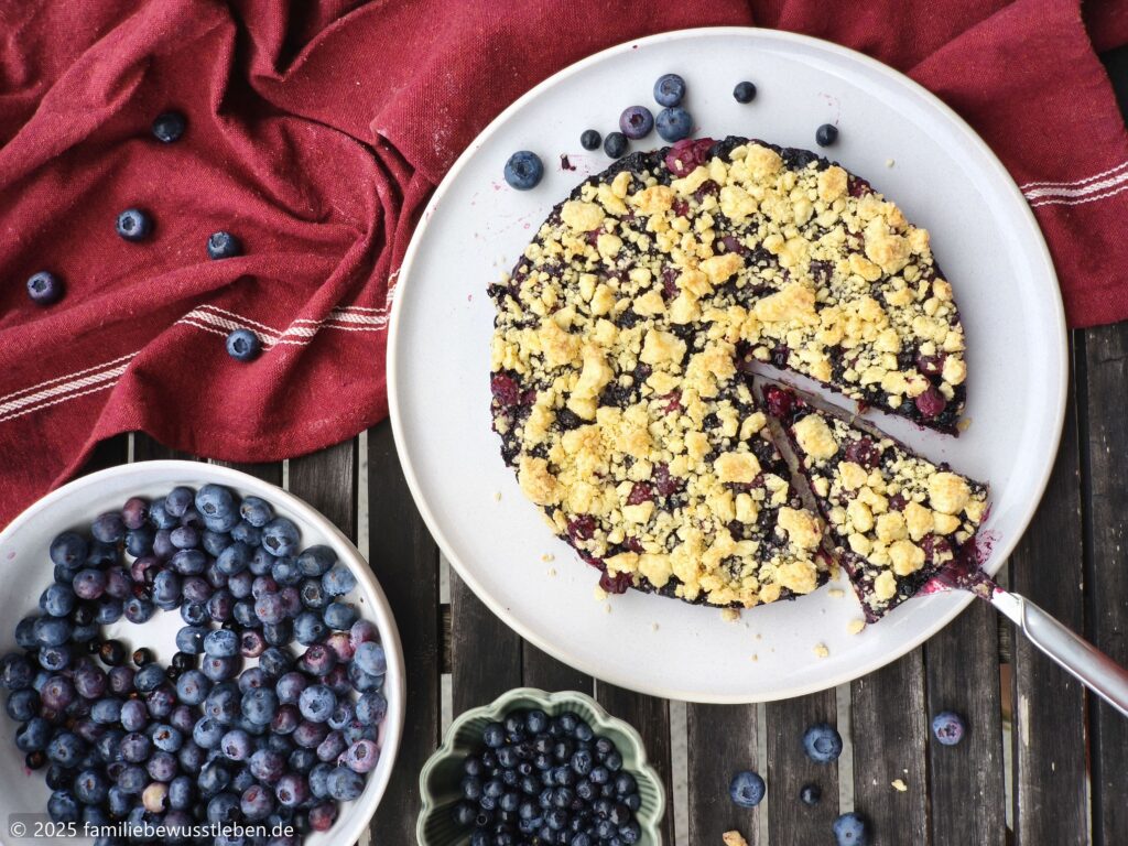 Heidelbeerkuchen und Blaubeeren in Schalen auf Tisch mit roten Küchentuch